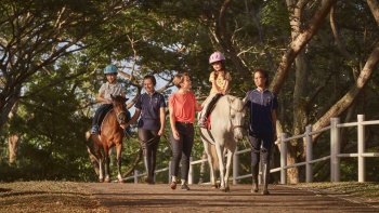 Eine Mutter und ihre Kinder reiten auf Ponys im Gallop Stable im Pasir Ris Park