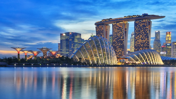 Abendansicht der Gardens by the Bay vor der Skyline der Marina Bay Singapore und mit dem Singapore River im Vordergrund