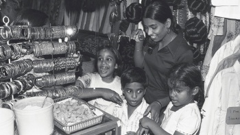 Ein Schwarz-Weiß-Foto einer jungen indischen Mutter mit ihren drei kleinen Kindern in einem Textil- und Schmuckgeschäft