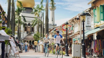 A couple cycling along the streets with Sultan Mosque featured in the background