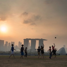 Boys playing soccer at Marina Barrage at dusk, with the misty silhouette of Marina Bay in the background