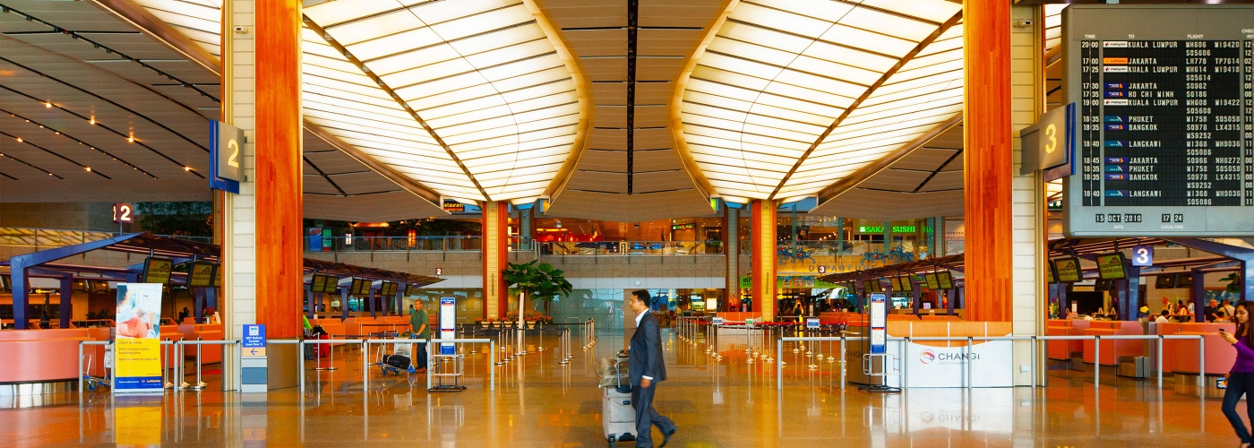 シンガポール・チャンギ空港の手荷物受付カウンターやチケットカウンターを、スーツケースを持って通り過ぎるスーツ姿の男性