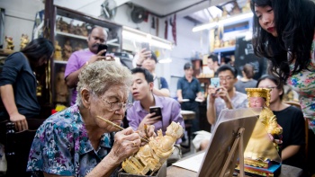 Người tham gia quan sát một thợ khắc điêu luyện ở Say Tian Hng Buddha Shop